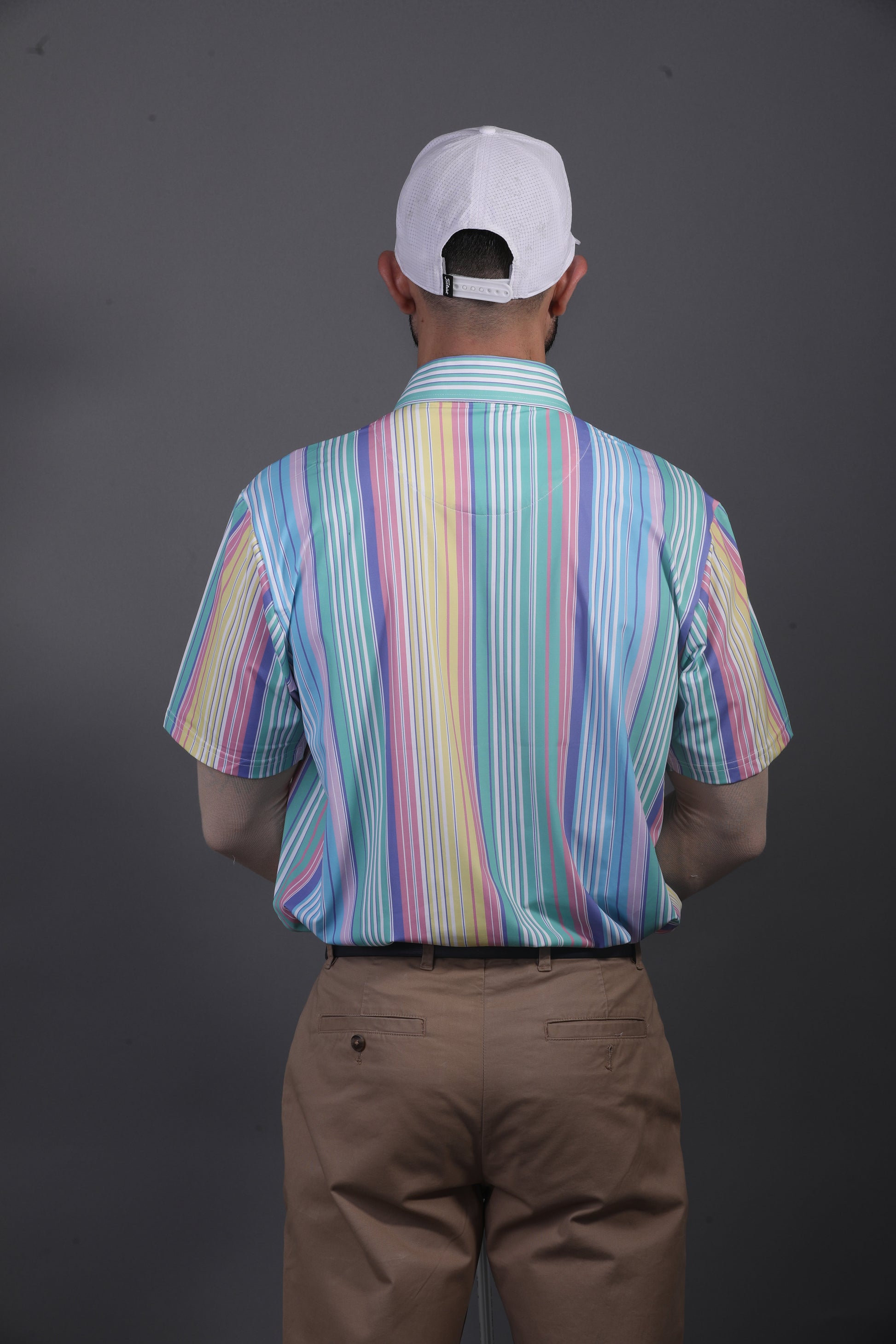 Person wearing a colorful striped shirt and white cap from behind on a dark background